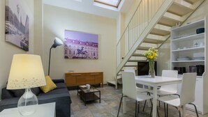 A modern living room with a sofa, a coffee table, a lamp, a dining table with chairs, a bookshelf, and a staircase. - Loft San Carlo by Wonderful Italy (Turin)