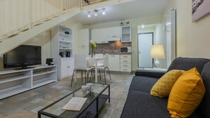 A modern living room with a flat-screen TV, a glass coffee table, a sofa with yellow cushions, and a staircase leading to an upper level. - Loft San Carlo by Wonderful Italy (Turin)