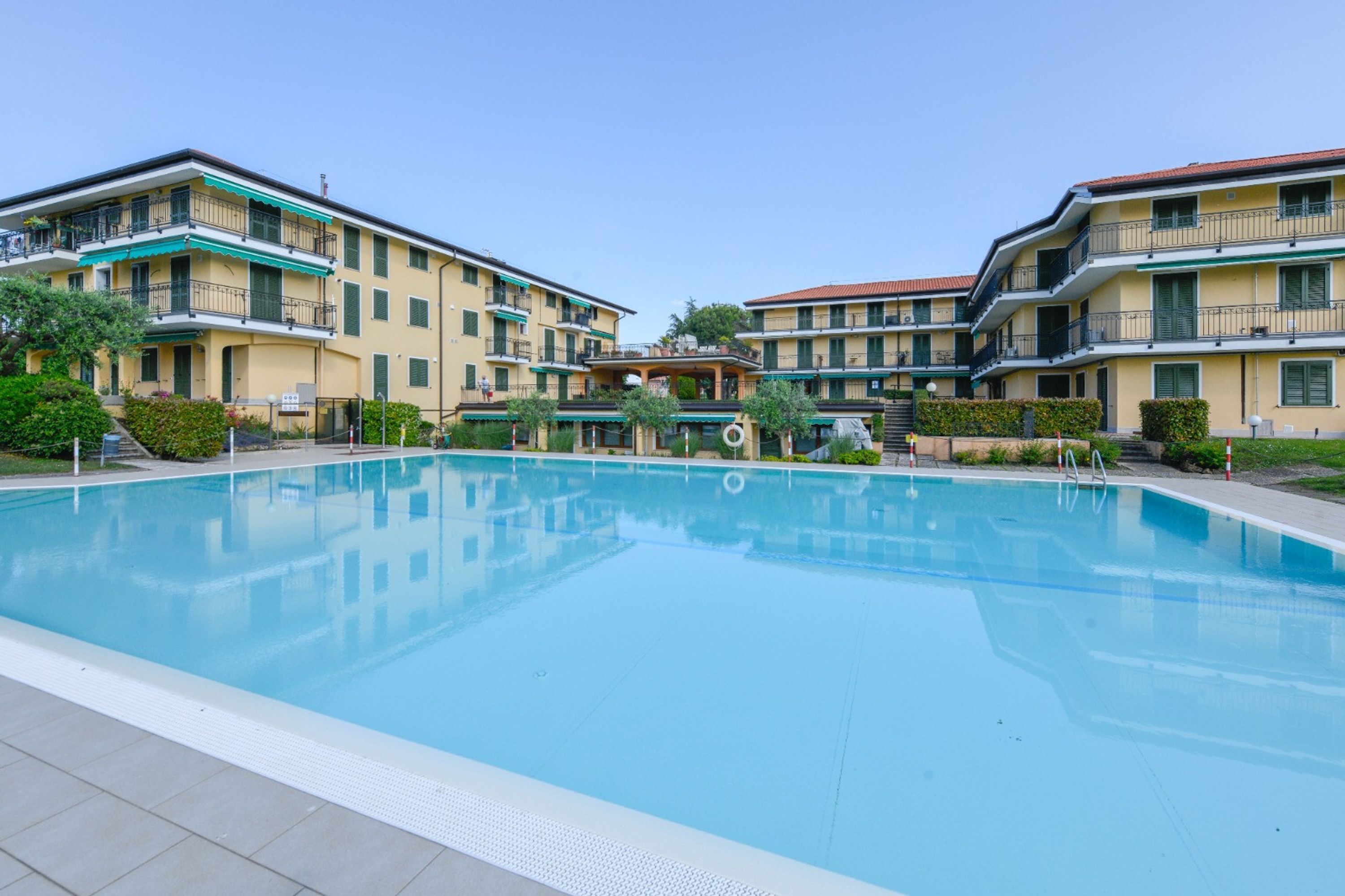 A swimming pool surrounded by multi-story buildings with balconies and a clear sky.