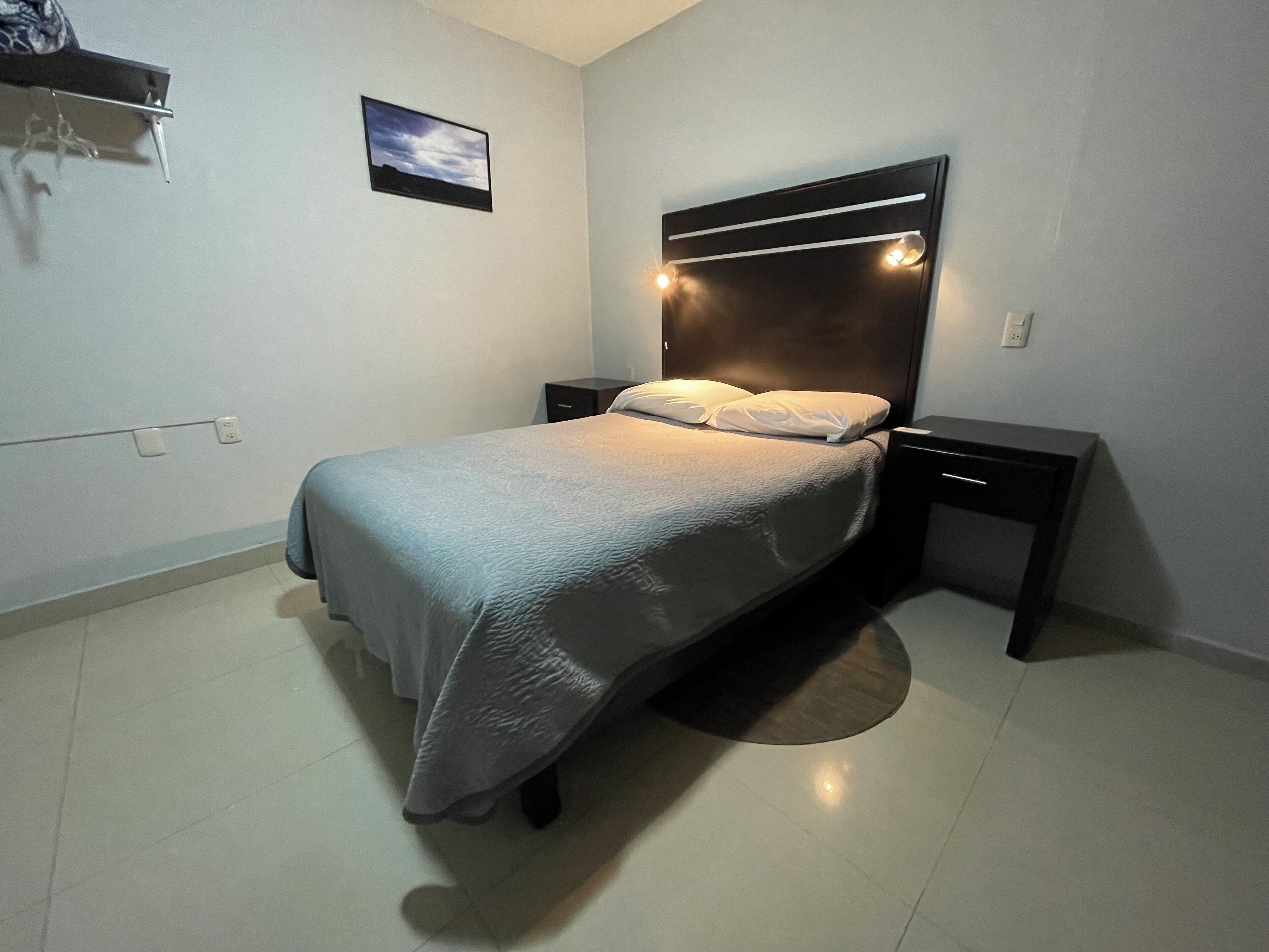 A neatly arranged bedroom with a bed, bedside tables, and a wall-mounted light fixture.