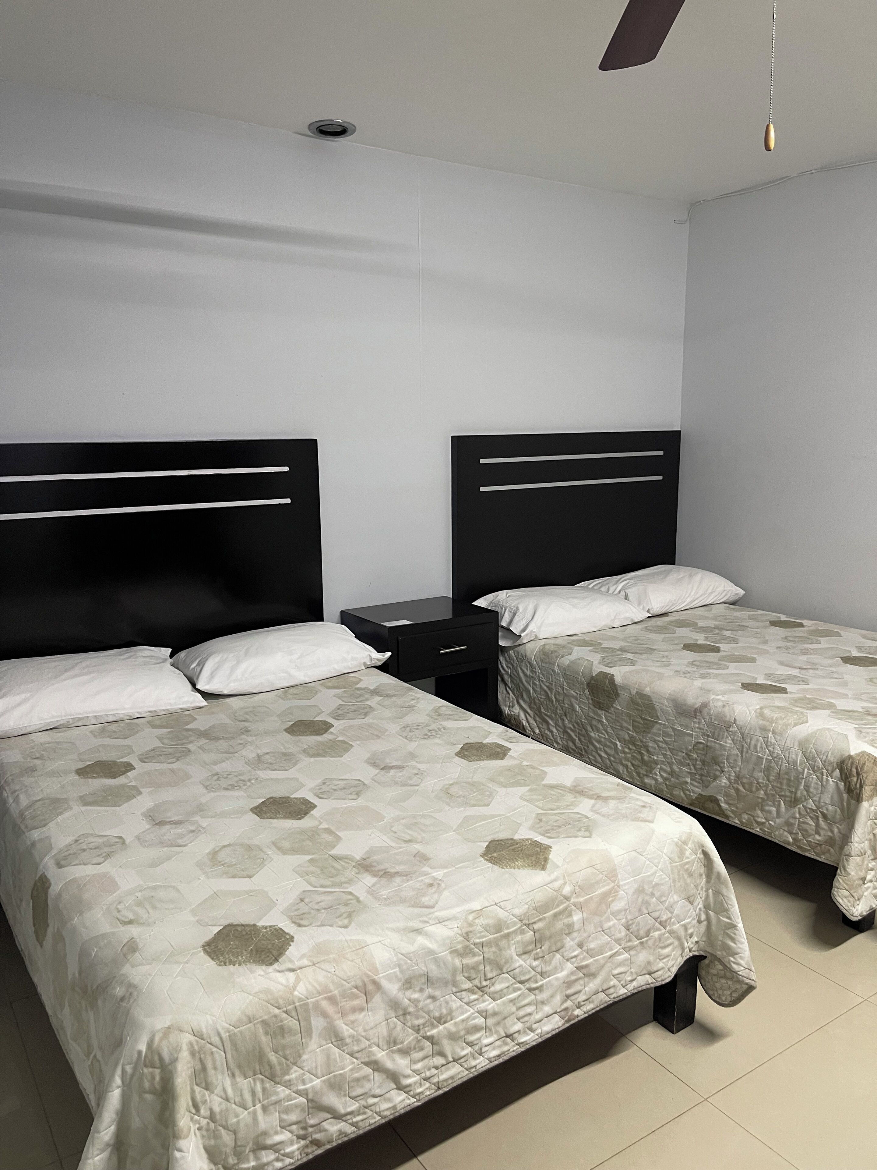 Quarto de hotel com duas camas, cada uma com cabeceira e mesa de cabeceira.