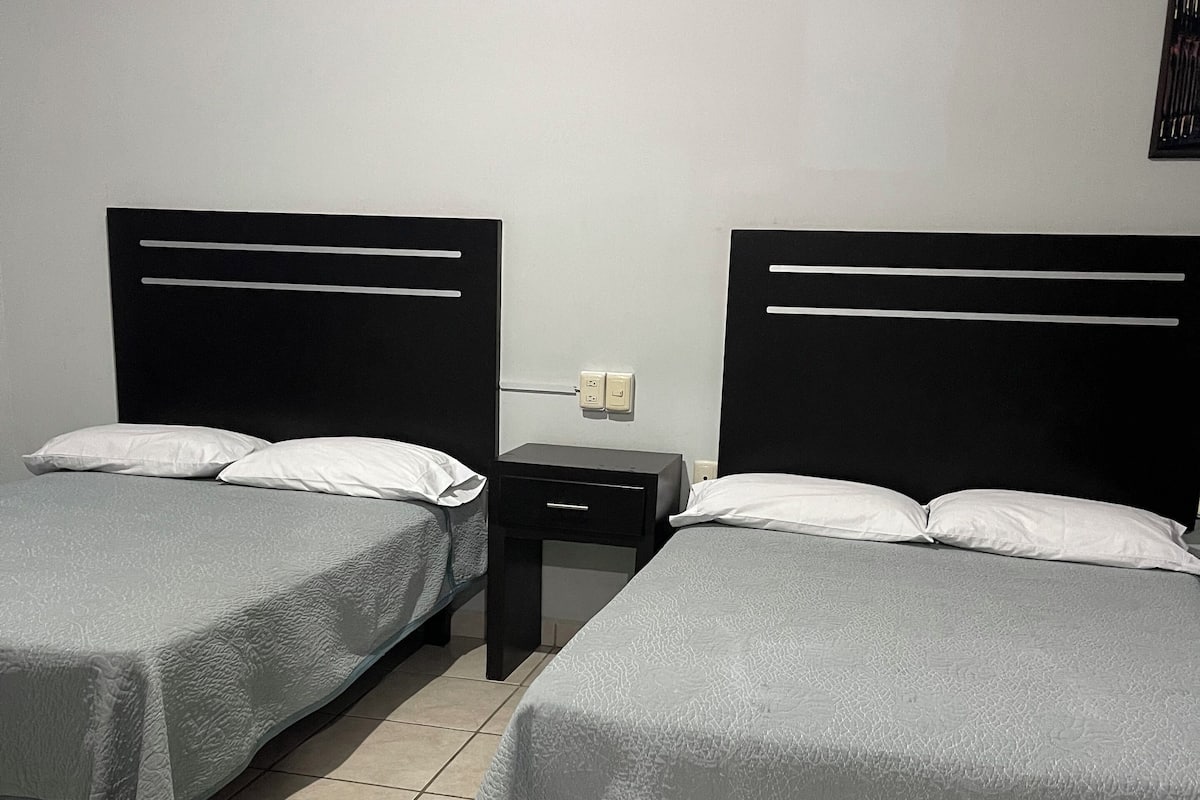 A hotel room with two beds, each with a headboard and a nightstand.