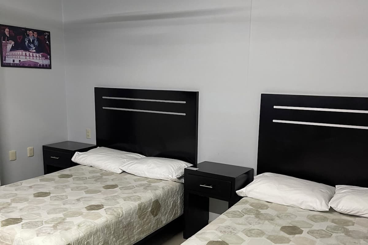 Two single beds with headboards, a nightstand, a ceiling fan, and a wall-mounted light fixture.