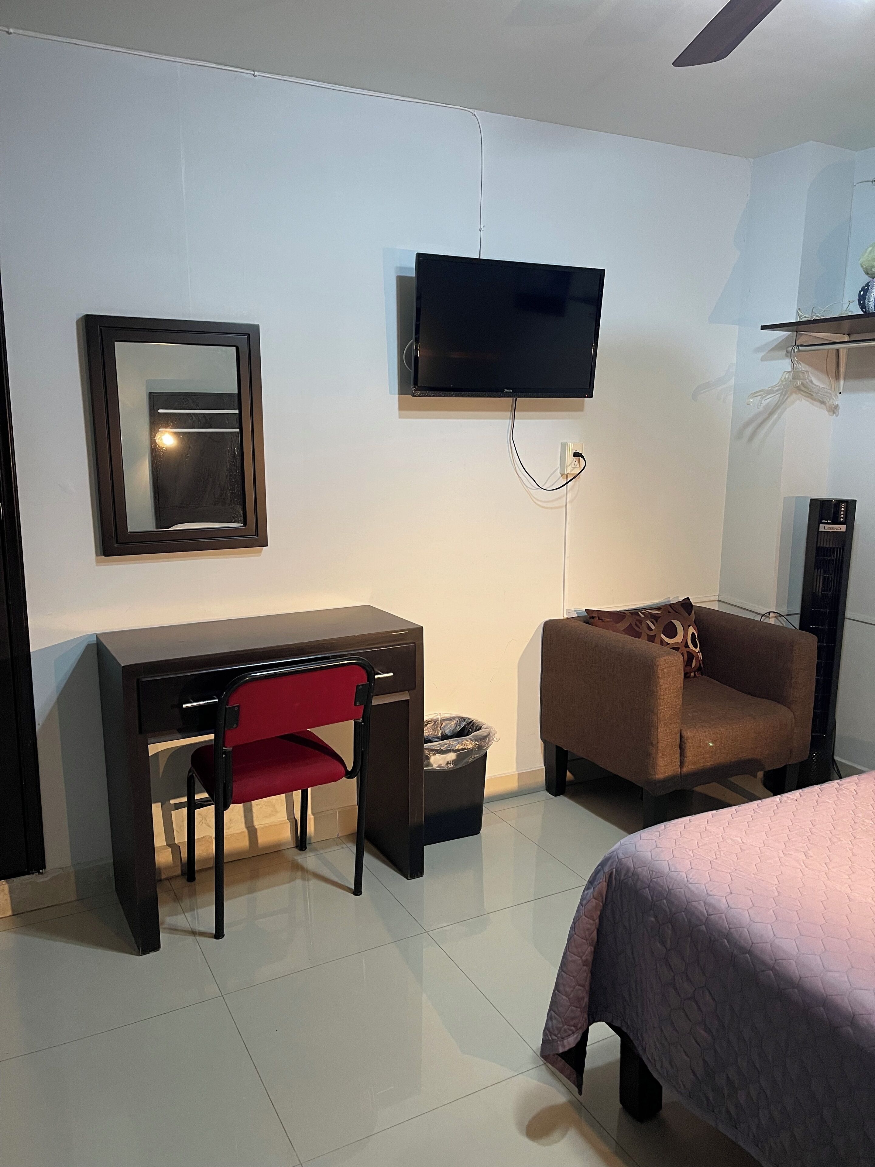Una habitación de hotel con escritorio, una silla, sofá, cama, televisor y ventilador de techo.