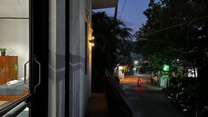 Un balcon donnant sur une rue la nuit, avec une moto et une devanture de magasin illuminée en vert.