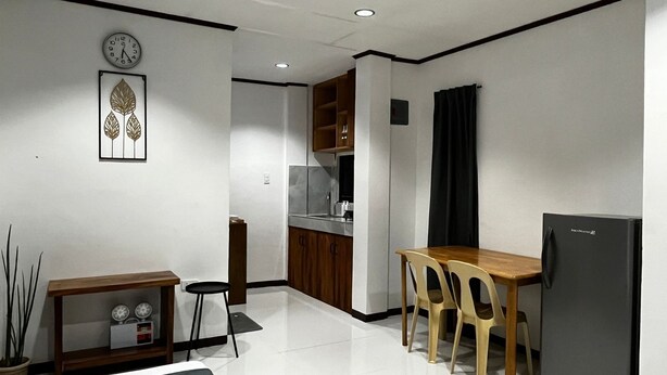 Une cuisine compacte avec un coin repas, comprenant une table en bois, des chaises, un réfrigérateur et une horloge murale.