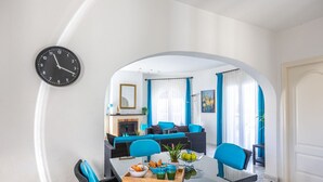 Un soggiorno moderno con zona pranzo, caratterizzato da un caminetto, arredi blu e una sveglia appesa al muro.