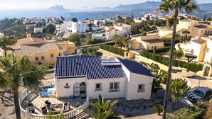 Una villa bianca con tetto in tegole, circondata da palme e una piscina, con vista su una località costiera.