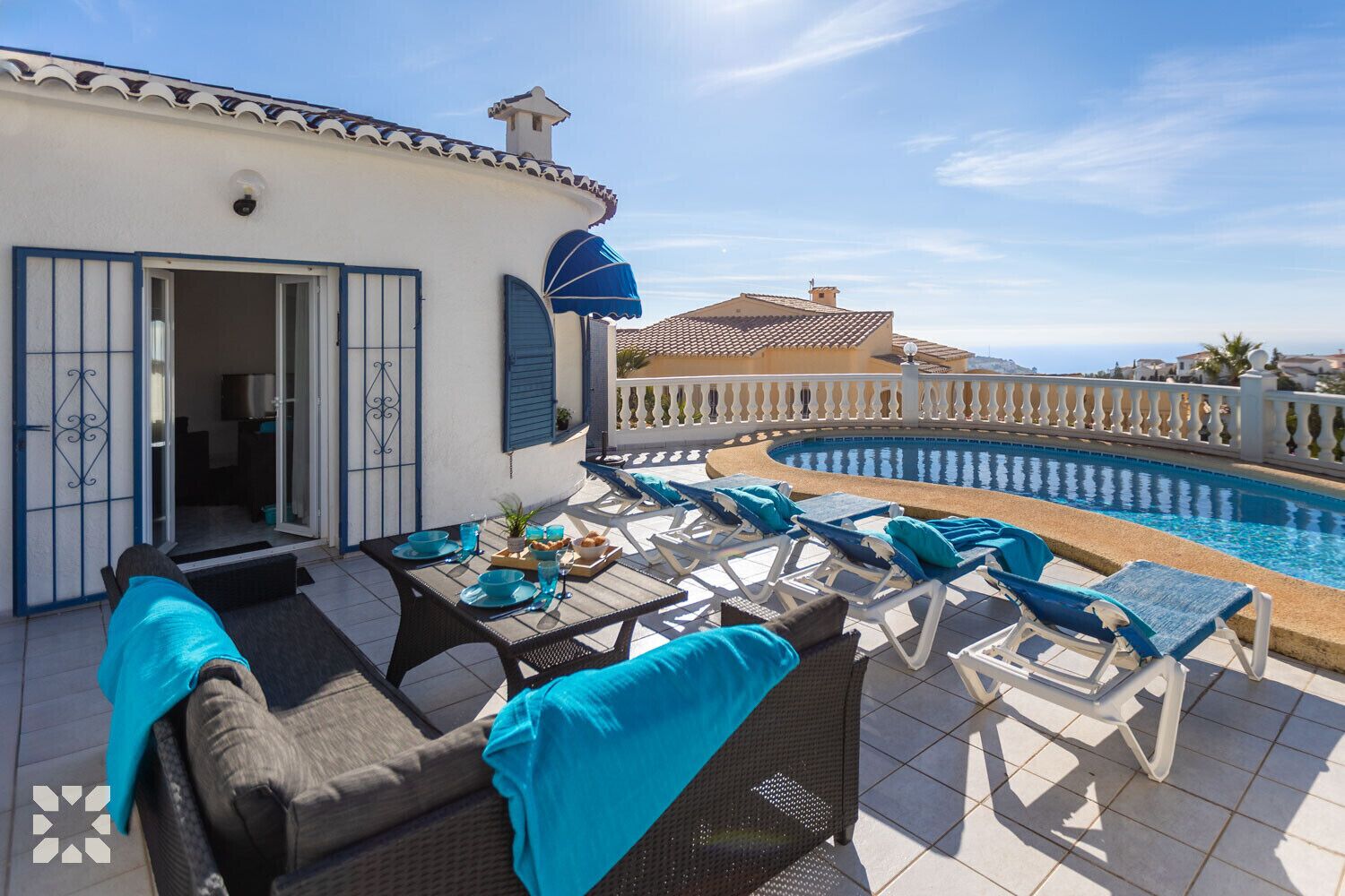 A terrace with a pool, lounge chairs, and a dining table set with blue tableware.