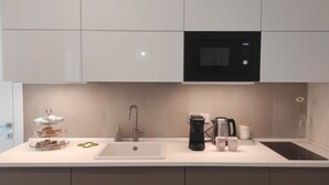 Eine moderne Küche mit weißer Arbeitsplatte, einer Edelstahl-Spüle, einer schwarzen Kaffeemaschine, einer Philips-Mikrowelle und einer zweistöckigen Glastheke mit Gebäck.