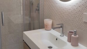 Ein modernes Badezimmer mit Duschkabine aus Glas, einem großen runden Spiegel und einem weißen Waschbecken mit Holdekor.
