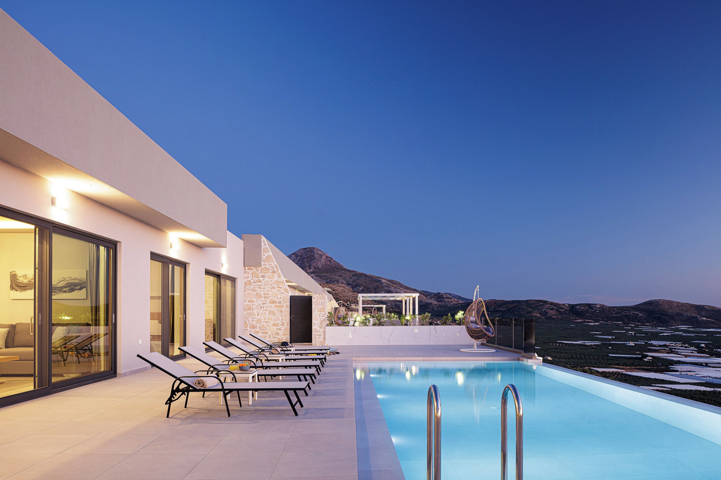 Un espace moderne aménagé au bord de la piscine, avec des chaises longues, une piscine et une vue sur les montagnes.