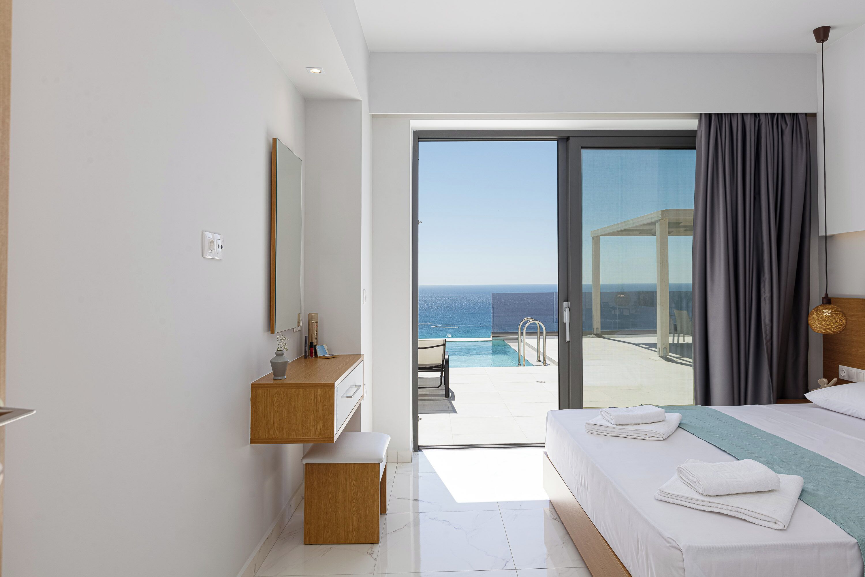 Une chambre d’hôtel moderne avec balcon, un lit, une table de chevet et vue sur l’océan.