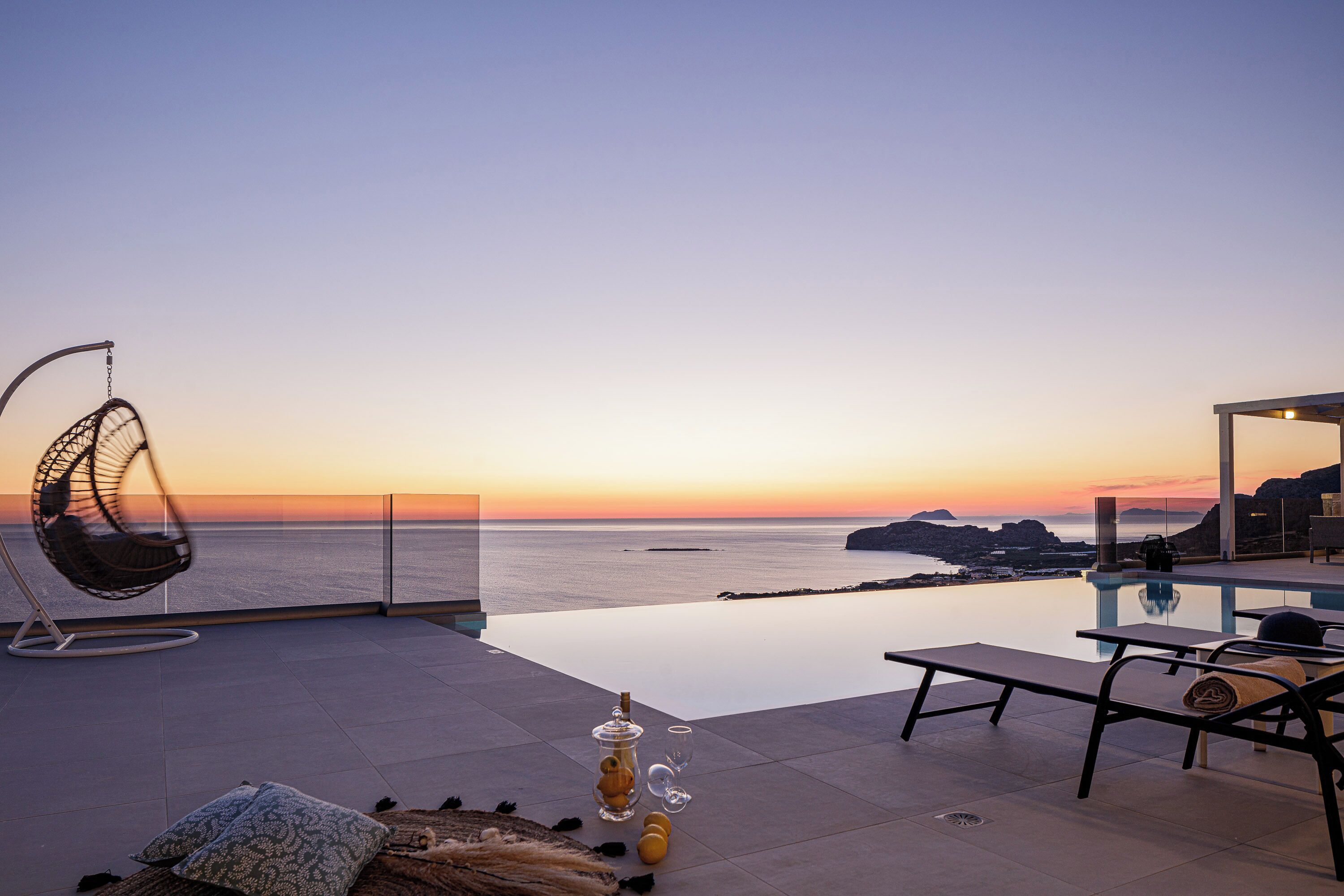 Une terrasse sur le toit, agrémentée d’un fauteuil suspendu, de chaises longues et d’une piscine à débordement offrant une vue imprenable sur la mer au coucher du soleil.