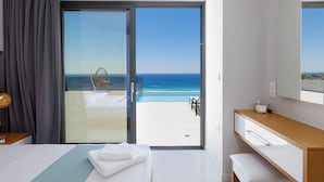 A modern hotel room with a large sliding glass door leading to a balcony with a pool and ocean view. - Falasarna Village  (Kissamos)