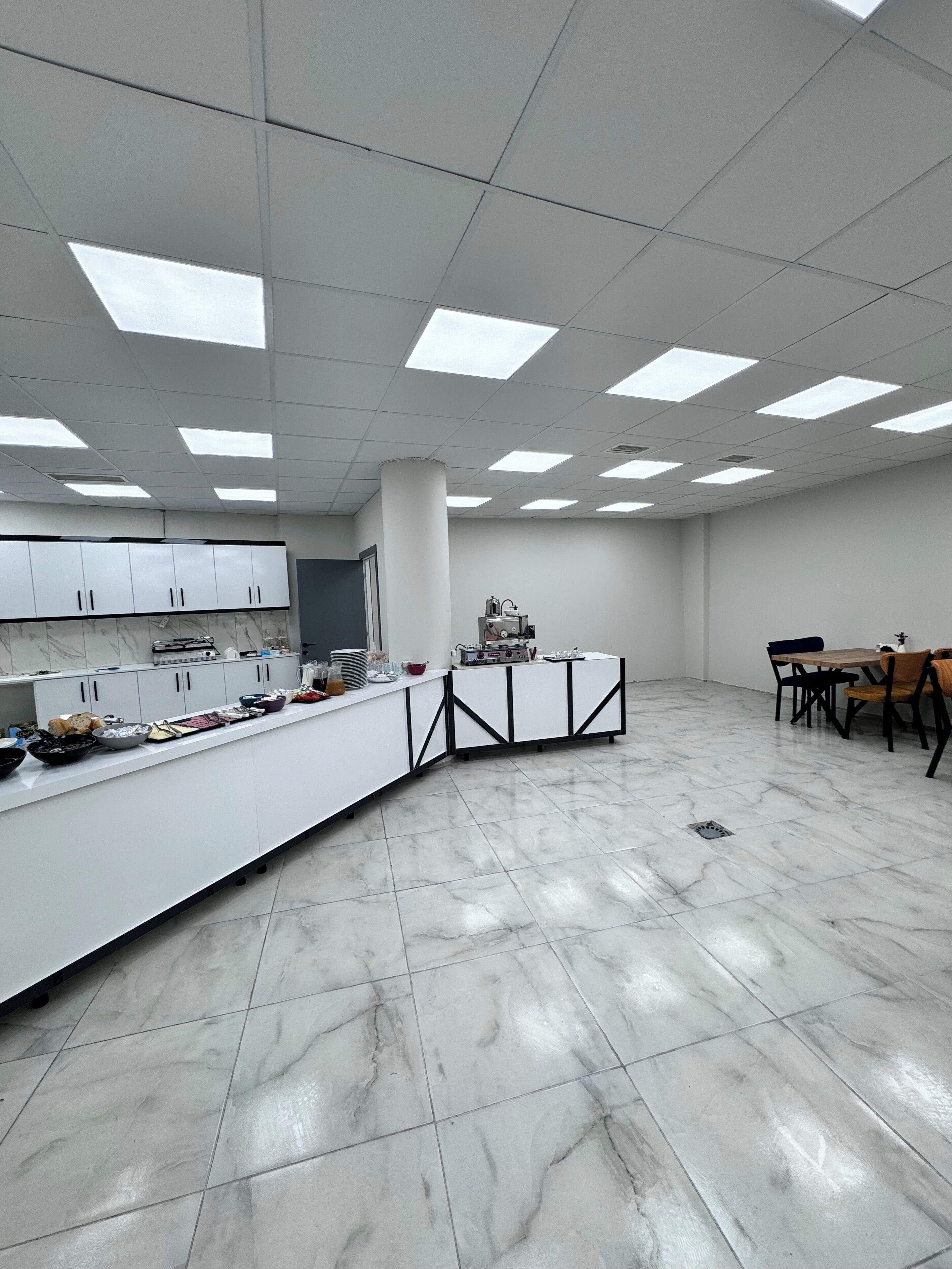 A spacious, well-lit kitchen with a marble floor, white cabinets, and a central island with various kitchen appliances and utensils.