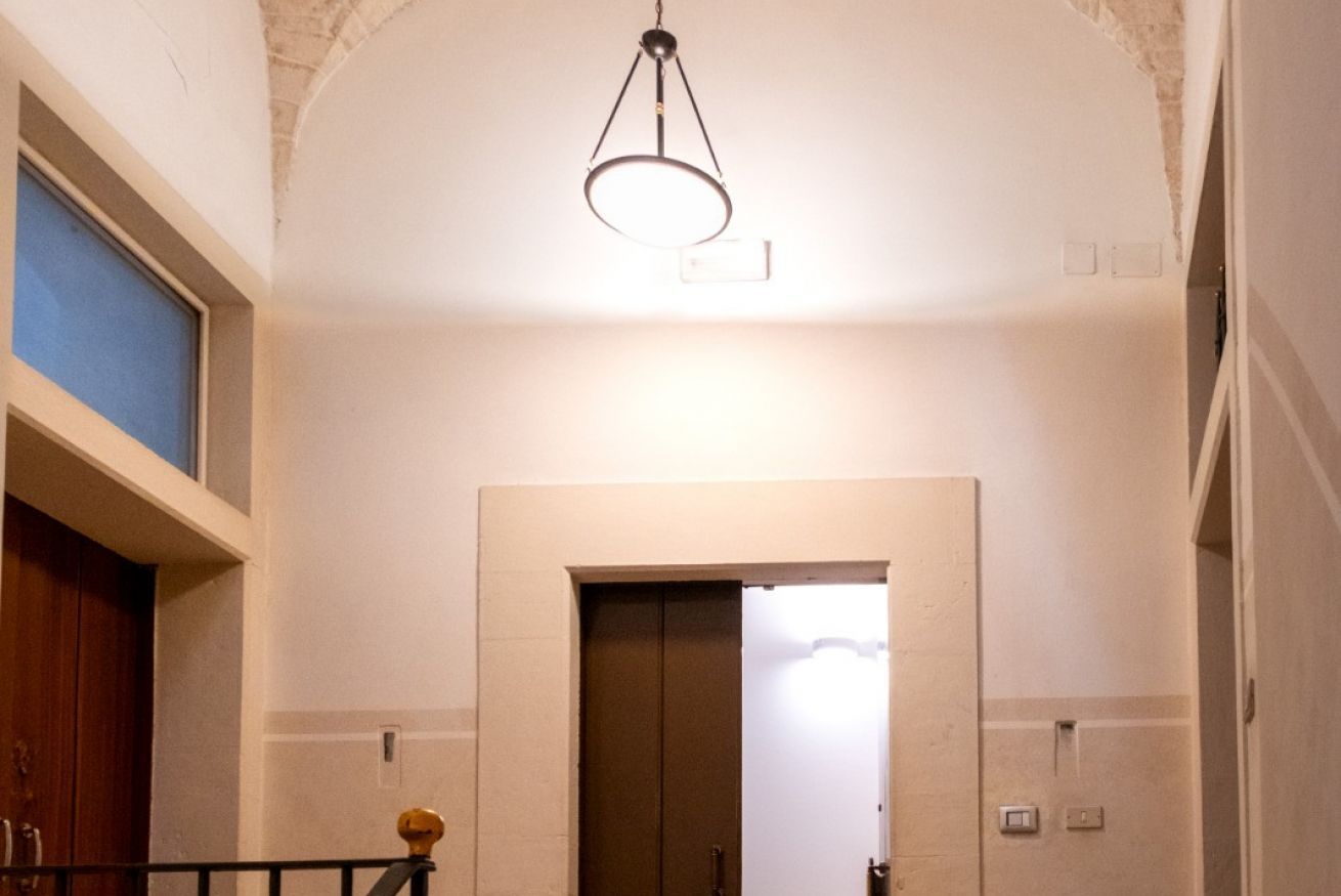 Un couloir avec une porte en bois, une rambarde en métal et un luminaire au plafond.