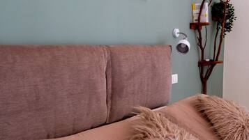 A room with a brown sofa, a fluffy throw, a wall-mounted lamp, and a plant on a wooden stand.