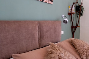 A room with a brown sofa, a fluffy throw, a wall-mounted lamp, and a plant on a wooden stand. - Le Gravinelle - Apulia Houses & Flats - Room 3 (Ruvo di Puglia)