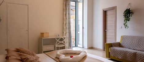 A bedroom with a bed, a desk, a chair, a sofa, and a door.