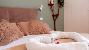 Een bed met een zacht wit kussen, een zachte witte deken, en een wit dierenbedje met een rood hart op een houten ondergrond.