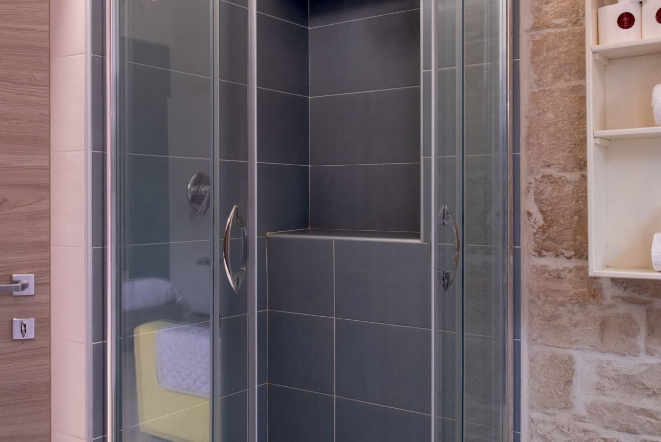 Un bagno moderno con cabina doccia in vetro, mobile lavabo in legno e parete in pietra.