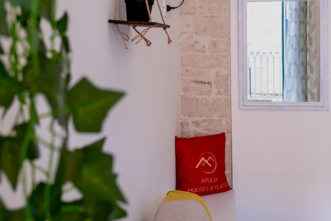 Une pièce avec un mur en briques, une fenêtre donnant sur une clôture, un coussin rouge orné d’un logo et une plante au premier plan.