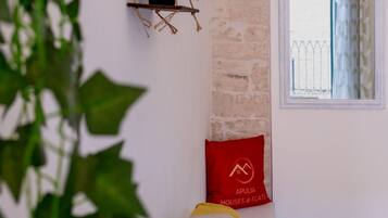 Une pièce avec un mur en briques, une fenêtre donnant sur une clôture, un coussin rouge orné d’un logo et une plante au premier plan.