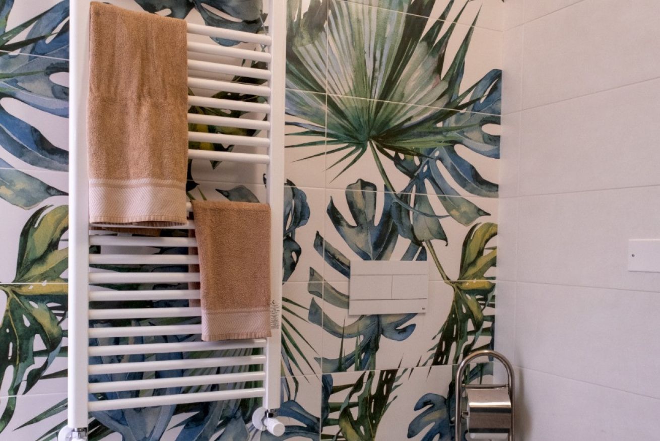 Een badkamer met een witte radiator, een handdoekhouder met twee handdoeken, en een muur met een tropisch bladmotief.