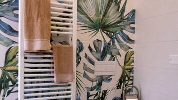 Een badkamer met een witte radiator, een handdoekhouder met twee handdoeken, en een muur met een tropisch bladmotief.