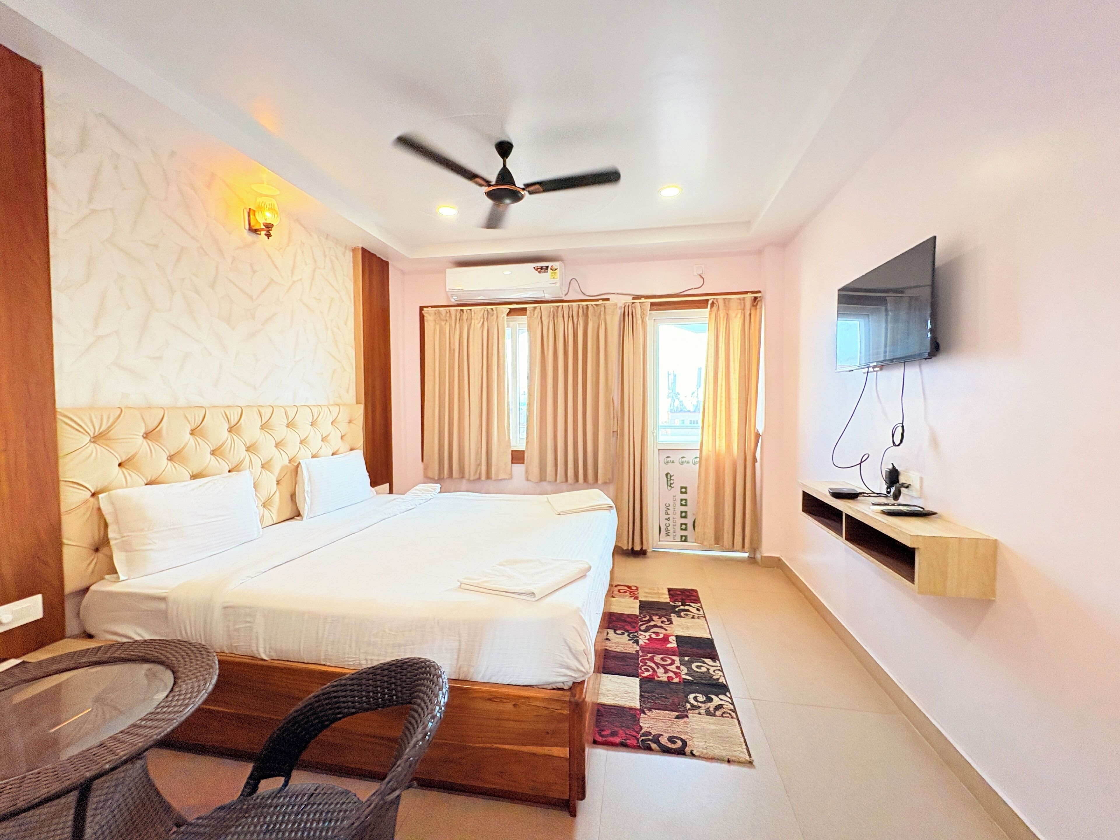 A hotel room with a large bed, a ceiling fan, a TV, and a small table with a chair.
