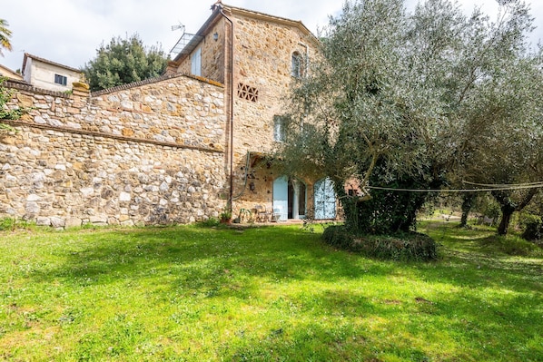 A stone building with a small porch, surrounded by greenery and trees.