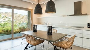 A modern kitchen with a large dining table, wicker chairs, and pendant lights. - Villa Elettra close to the sea - My Rental Homes (Mykonos)