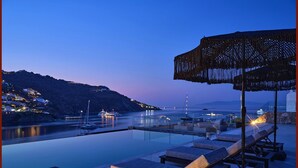 An infinity pool with lounge chairs and a pergola overlooking a coastal area with boats and buildings. - Villa Elettra close to the sea - My Rental Homes (Mykonos)