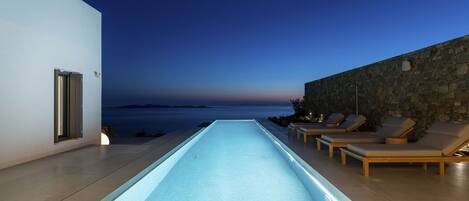 A modern infinity pool with a view of the sea at dusk.