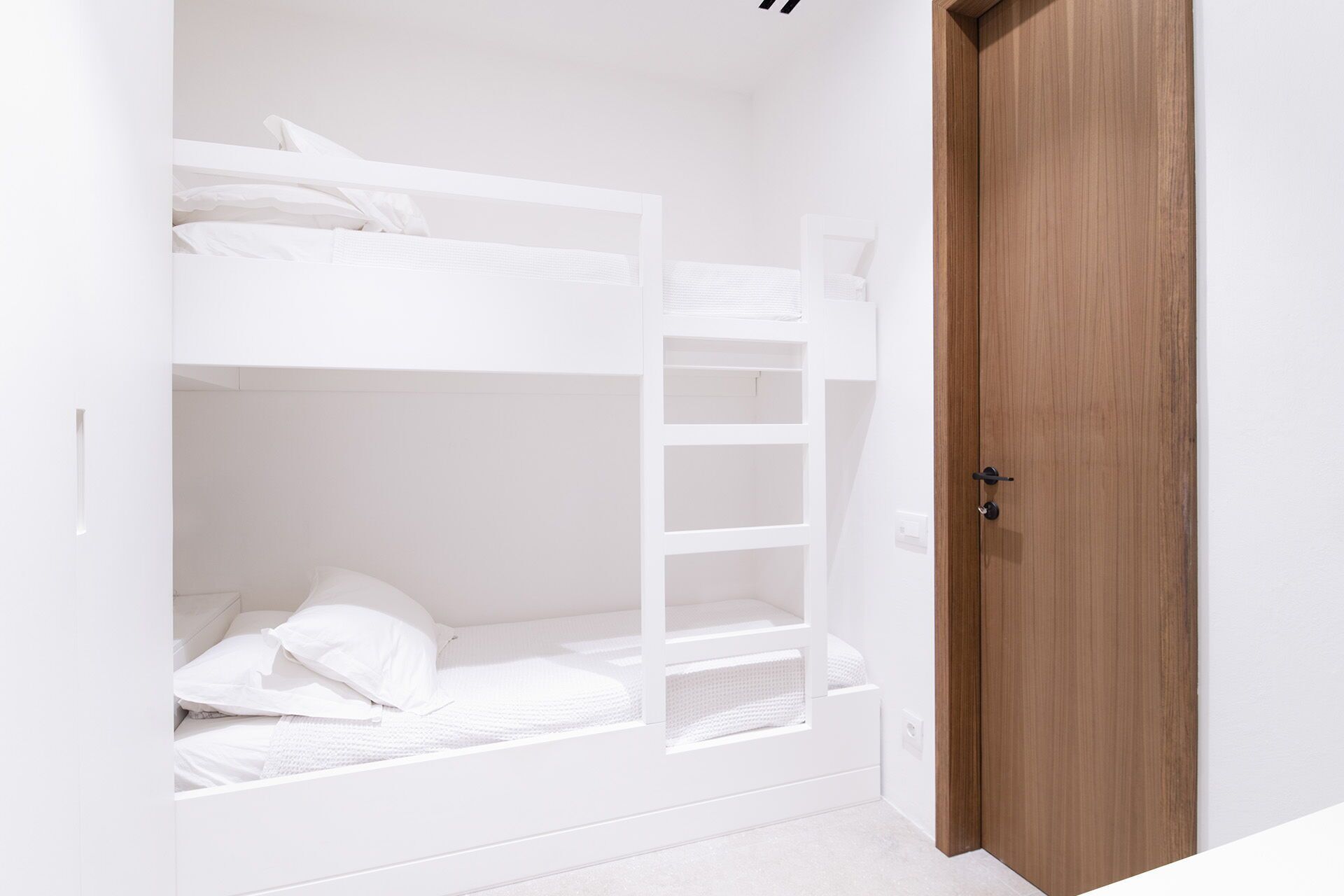 A bunk bed with white bedding and a wooden door.