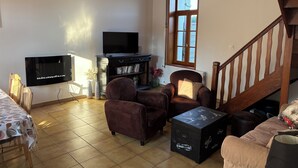Een woonkamer met een televisie, twee bruine fauteuils, een salontafel en een trap.