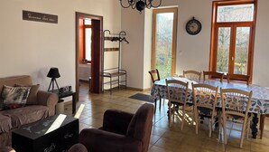 Een gezellige woonkamer met een bank, een salontafel, een eettafel met stoelen, een kroonluchter en een kapstok.