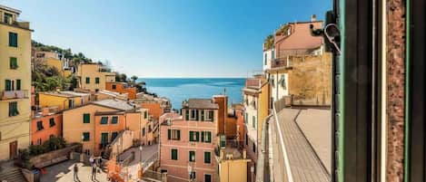 Uma vila costeira com edifícios coloridos, vista clara do mar e uma área pedonal com degraus que descem até à orla marítima.