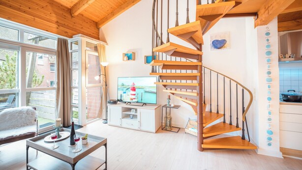 Ein modernes Wohnzimmer mit einer Holztreppe, einem Fernseher und einem Essbereich mit Tisch für zwei Personen.