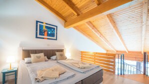 Ein modernes Schlafzimmer mit schrägen Wänden, einem großen Bett, ordentlich gefalteten Handtüchern, einem Nachttisch mit Lampe und einem Gemälde an der Wand.