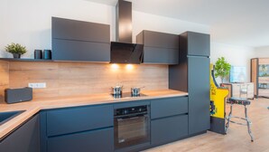 Une cuisine moderne avec des meubles de couleur sombre, un plan de travail en bois et des appareils électroménagers intégrés, notamment un lave-vaisselle et un four.