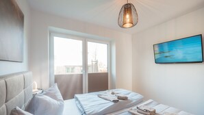 Une chambre à coucher moderne avec une grande fenêtre, un lit sur lequel sont soigneusement pliées des serviettes, et un tableau accroché au mur.