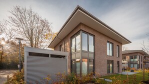 Une maison moderne à deux étages, avec une façade en briques, de grandes fenêtres et une porte de garage.