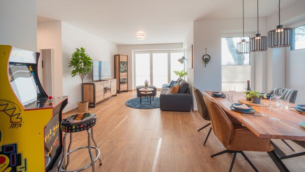 Un salon spacieux avec une table à manger en bois, un canapé et un téléviseur. On y trouve également une plante, une lampe et une console de jeux.