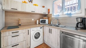 Una cocina compacta equipada con lavadora, microondas, lavaplatos y cafetera.