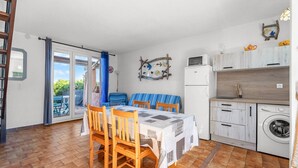 Cocina compacta con zona de comedor, lavadora y vistas a través de la puerta de cristal.