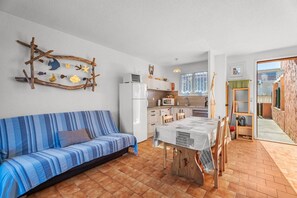 A compact living space with a sofa, a dining table, a kitchen area, and a view of the outside. - Holiday Home “Near the Beach” with Sea View (Six-Fours-les-Plages)