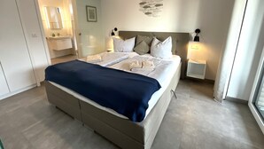 A modern bedroom with a large bed, bedside tables, a wall-mounted artwork, and a sliding door leading to a bathroom. - Hello and welcome to Nordseeliebe! (Dangast)