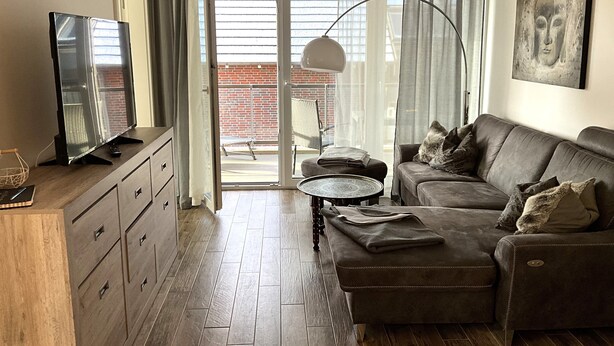 A living room with a sofa, a television, a coffee table, and a view of a balcony. - Moin and welcome to Apartment Küstenglück! (Dangast)